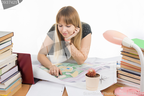 Image of A girl student with a smile looks at a drawing master plan at a table cluttered with books