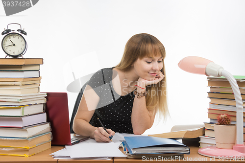 Image of Pretty teenage girl has been at the table cluttered with books in the library