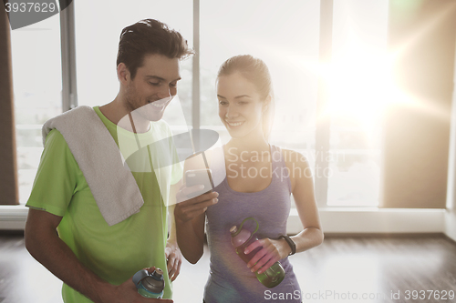 Image of happy woman and trainer showing smartphone in gym