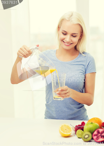 Image of smiling woman pouring fruit juice to glass at home