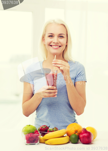 Image of smiling woman drinking fruit shake at home