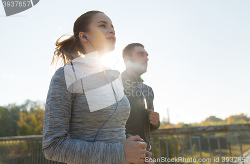 Image of happy couple with earphones running outdoors