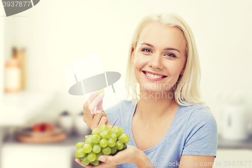 Image of happy woman eating grapes on kitchen
