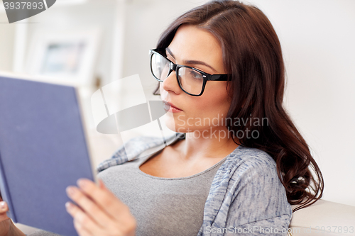 Image of young woman in glasses reading book at home