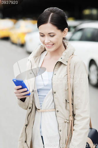 Image of smiling woman with smartphone over taxi in city