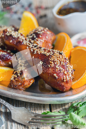 Image of Fried chicken drumsticks with sesame seeds and orange slices.
