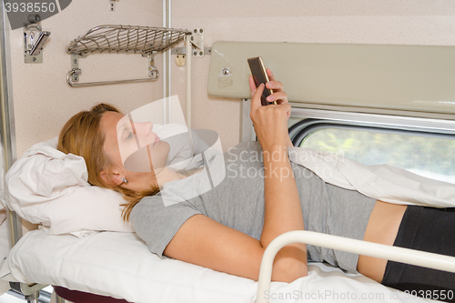 Image of The girl on the train lying on his back on the top shelf in the side car with reserved seats and looking at the phone