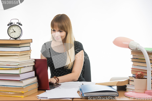 Image of The girl behind the desk littered with books smiling in a laptop information gathering