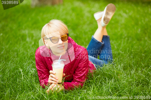 Image of Beautiful young woman enjoys drinking coffee and lying on the grass