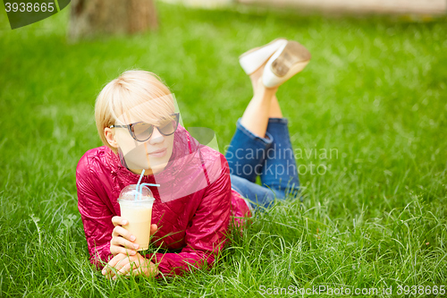 Image of Beautiful young woman enjoys drinking coffee and lying on the grass