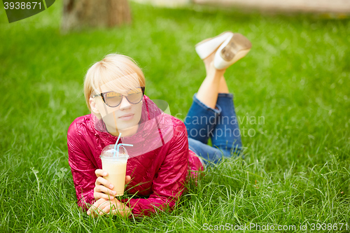 Image of Beautiful young woman enjoys drinking coffee and lying on the grass