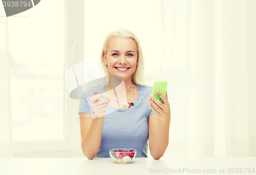 Image of woman with smartphone eating fruits at home