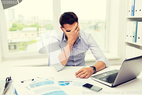 Image of businessman with laptop and papers in office