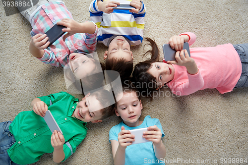 Image of happy children with smartphones lying on floor