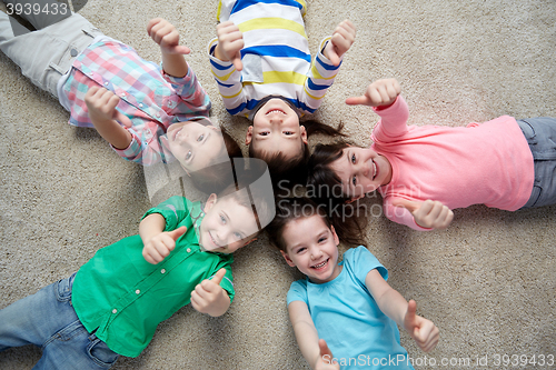 Image of happy kids lying on floor and showing thumbs up