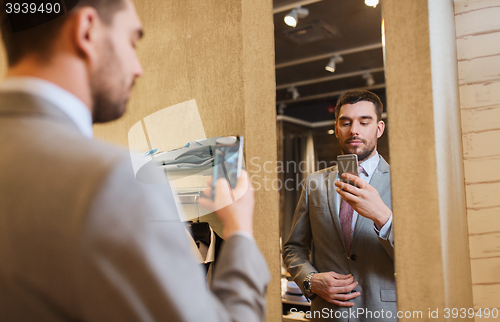 Image of man in suit taking mirror selfie at clothing store