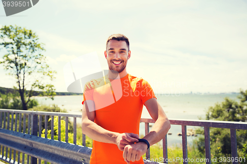 Image of smiling young man with smart wristwatch at seaside