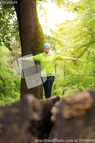 Image of Woman holding balance on tree trunk in nature.