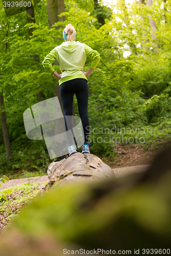 Image of Woman standing on tree trunk in nature.