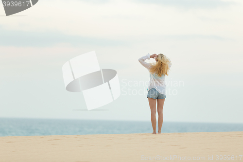 Image of Woman on sandy beach in white shirt at dusk. 