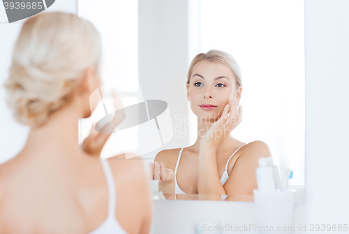 Image of happy woman applying cream to face at bathroom