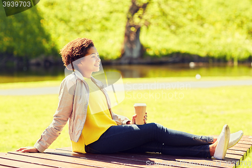 Image of happy african woman drinks coffee at summer park 