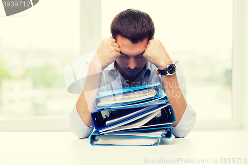 Image of sad businessman with stack of folders at office