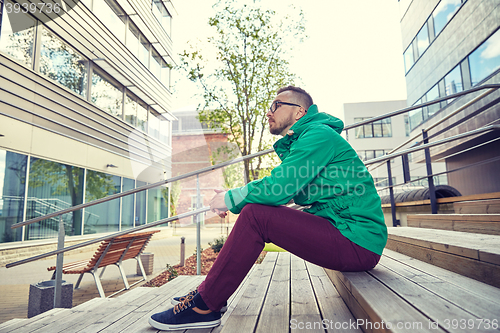 Image of happy young hipster man sitting on stairs in city