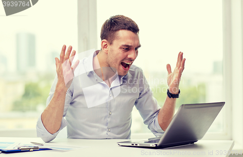 Image of angry businessman with laptop and papers in office