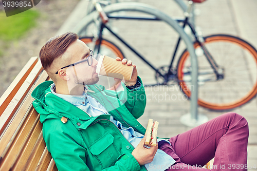 Image of happy young hipster man with coffee and sandwich