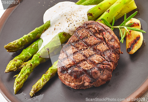 Image of grilled beef steak and asparagus on dark plate