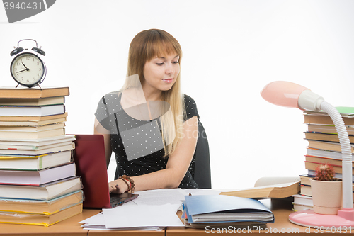 Image of college student smiling with a laptop in gaining information while sitting at a table littered with books in the library