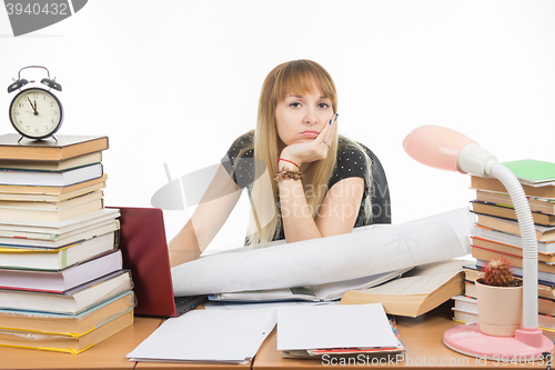 Image of Girl student sitting sadly at the table crammed with books and papers