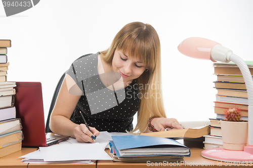 Image of A student at a table littered with books in the library happily writes synopsis