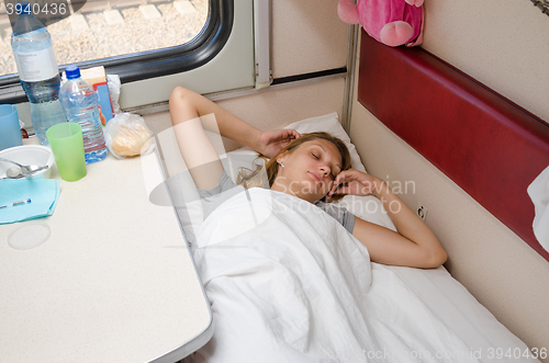 Image of Girl sleeps in train arms outstretched on the lower second-class place car coupe