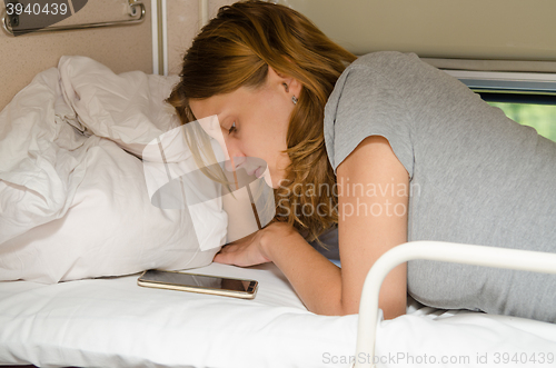 Image of Passenger train lying on his stomach on the top shelf in a second-class carriage and looking at the phone