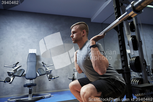 Image of young man flexing muscles with barbell in gym