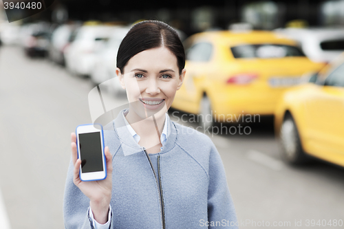 Image of smiling woman showing smartphone over taxi in city