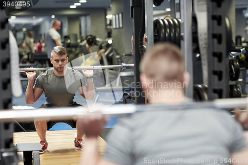 Image of young man flexing muscles with barbell in gym