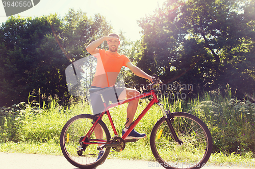 Image of happy young man riding bicycle outdoors