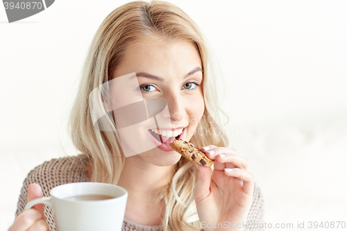 Image of happy woman with tea eating cookie at home