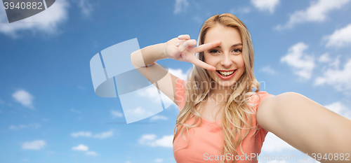 Image of smiling woman taking selfie and showing peace sign