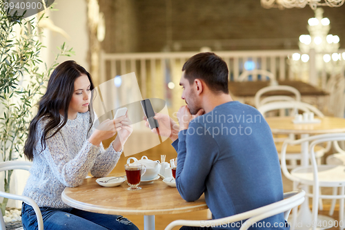 Image of couple with smartphones drinking tea at cafe