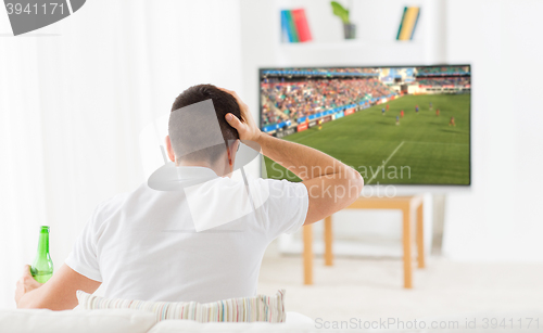 Image of man watching football or soccer game on tv at home