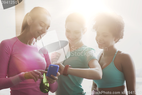 Image of happy women showing time on wrist watch in gym