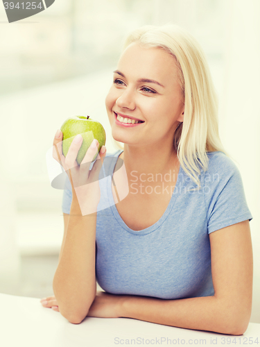 Image of happy woman eating green apple at home