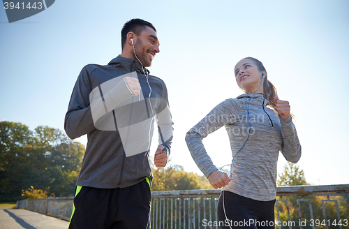 Image of happy couple with earphones running outdoors