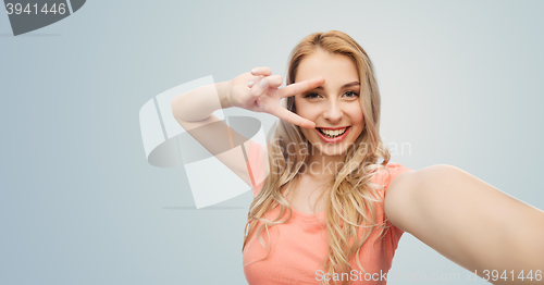 Image of smiling woman taking selfie and showing peace sign