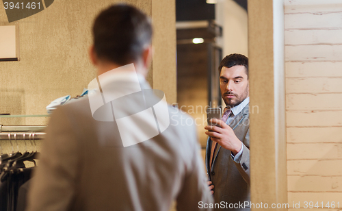 Image of man in suit taking mirror selfie at clothing store