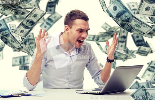 Image of angry businessman with laptop and falling money